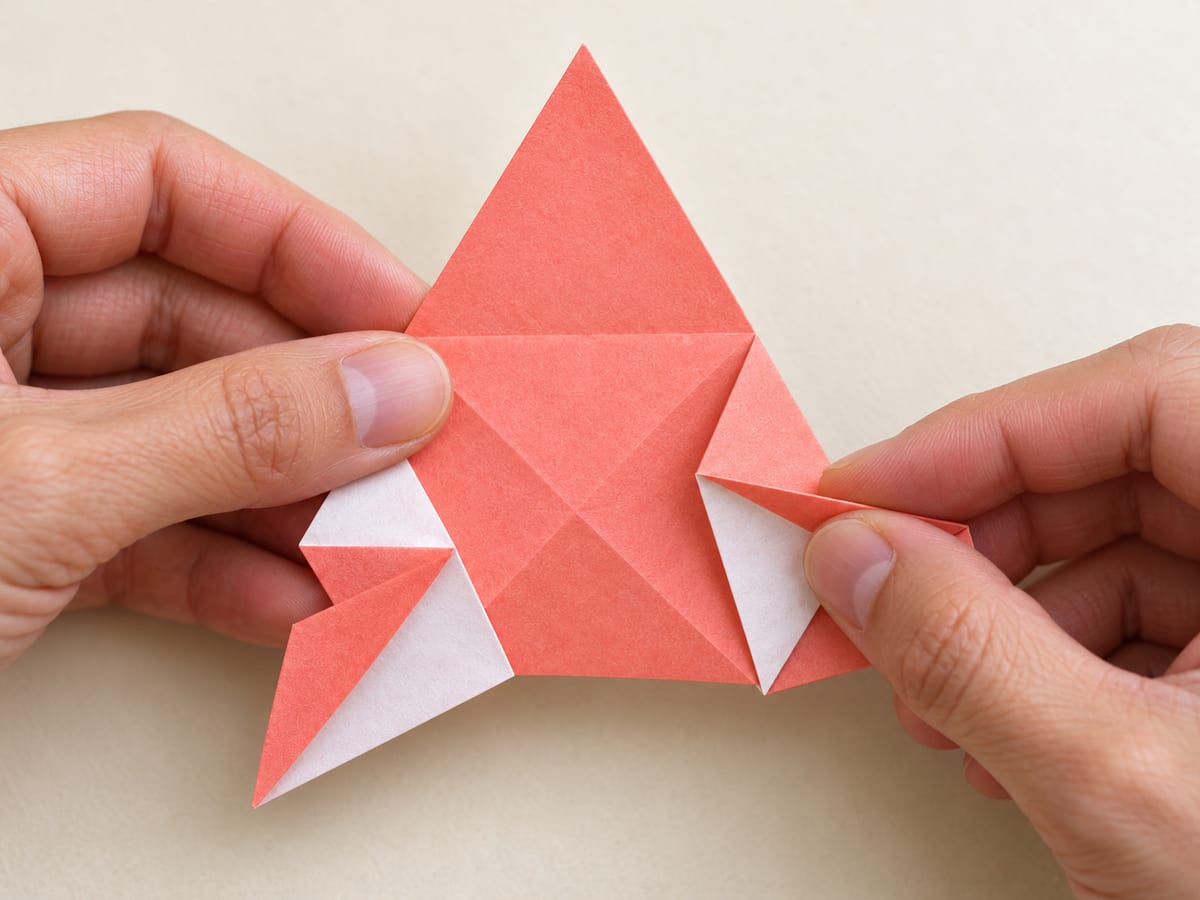 origami star step 11: pleat each corner along its two guide lines, folding outward at the outer line and inward at the inner line, hands visible