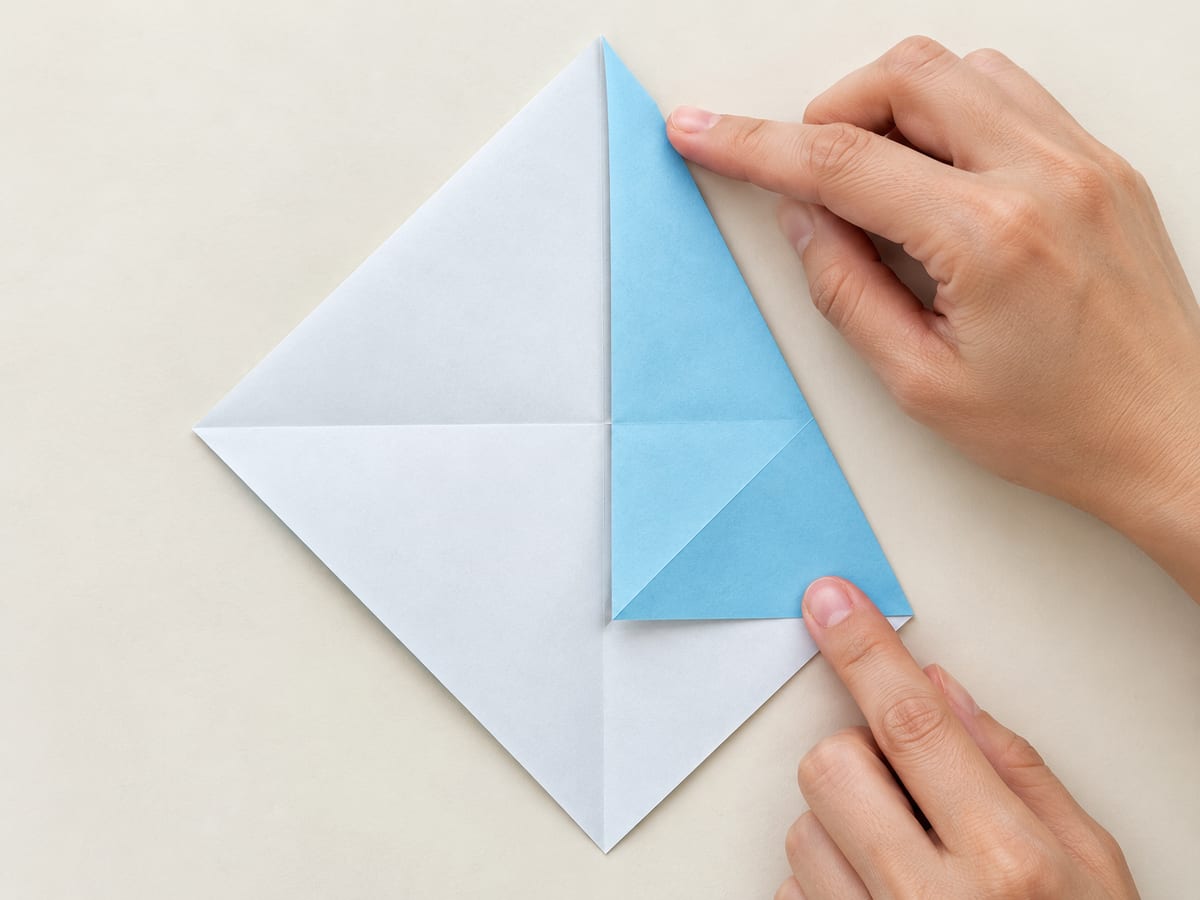 origami shark step 3: fold the upper-right sloping edge inward to the vertical center crease, hands visible