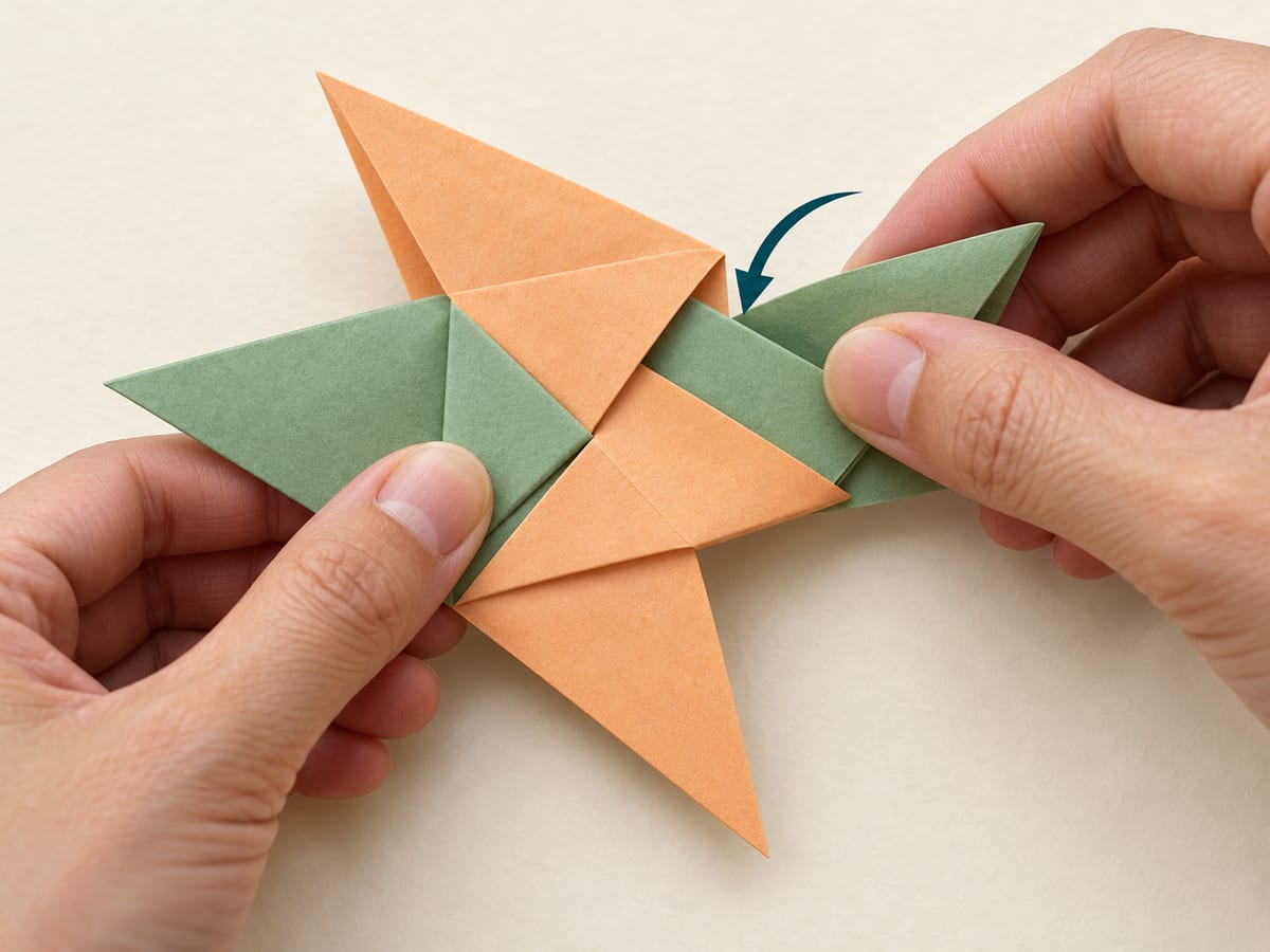 origami ninja star step 10: fold the two exposed points of the lower piece across the center and slide them into the upper piece pockets, hands visible