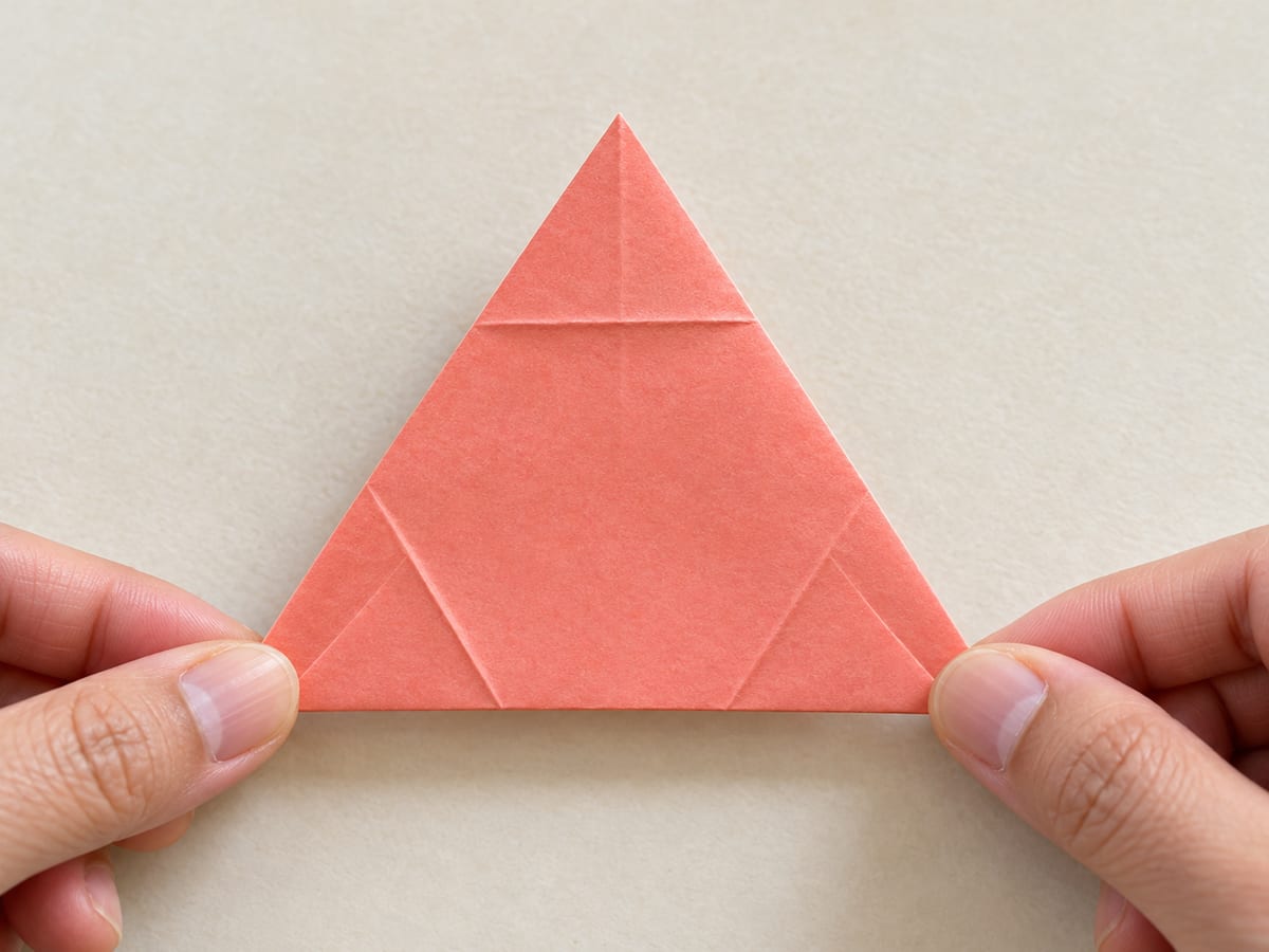 origami star step 10: turn the triangle over again, exposing the outer and inner crease pairs, hands visible