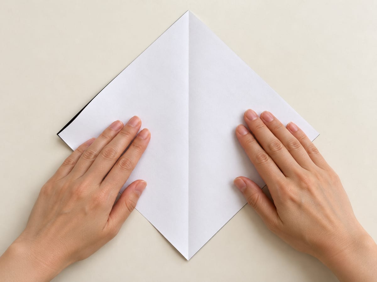 origami penguin step 1: place the square as a diamond; fold the left corner to the right, crease, reopen, and turn over, hands visible