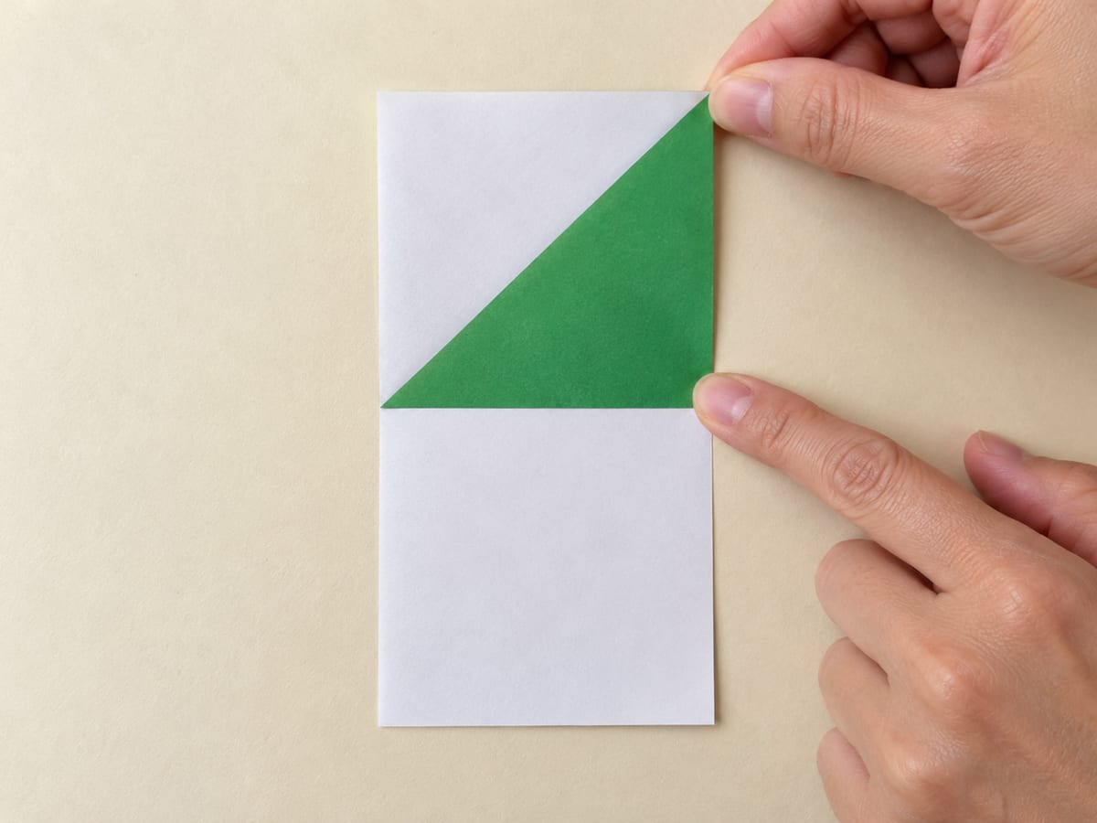 origami frog step 2: bring the upper-left corner to the right edge, aligning the top edge with that side; crease and unfold, hands visible