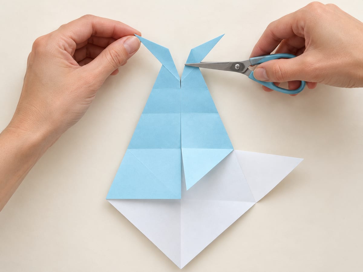 origami shark step 9: snip the narrow top tip to the nearest horizontal guide and fold both tail tips outward, hands visible