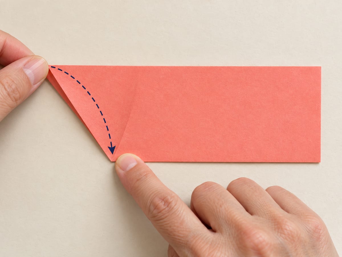 origami star step 3: fold the upper-left sloping edge down to meet the bottom long edge, forming an equal-sided triangle, hands visible