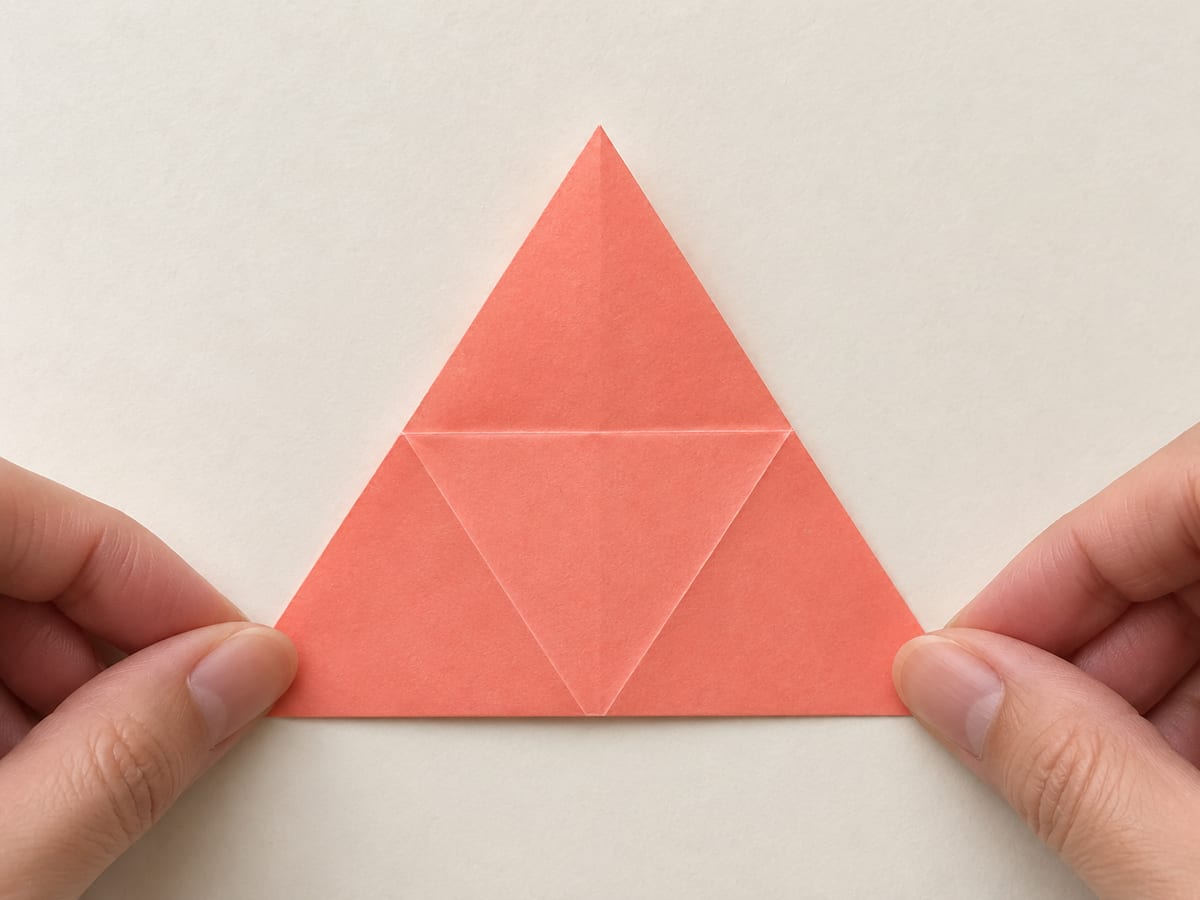 origami star step 8: turn the triangle over, keeping one corner at the top, hands visible