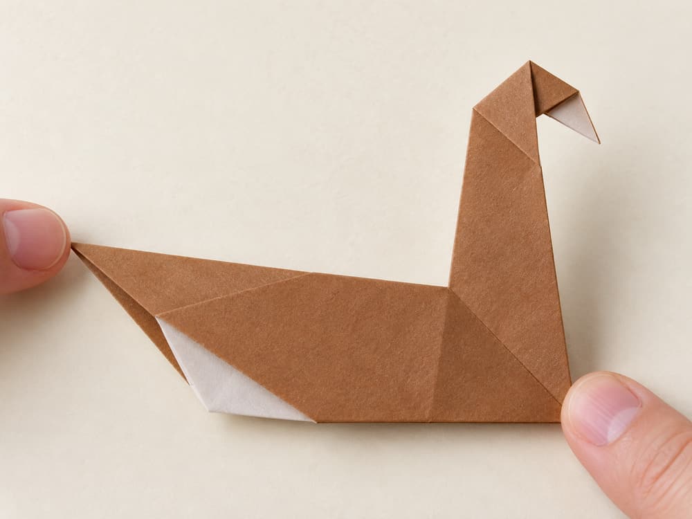 origami turkey step 8: fold the neck tip downward to make a short head and beak, hands visible