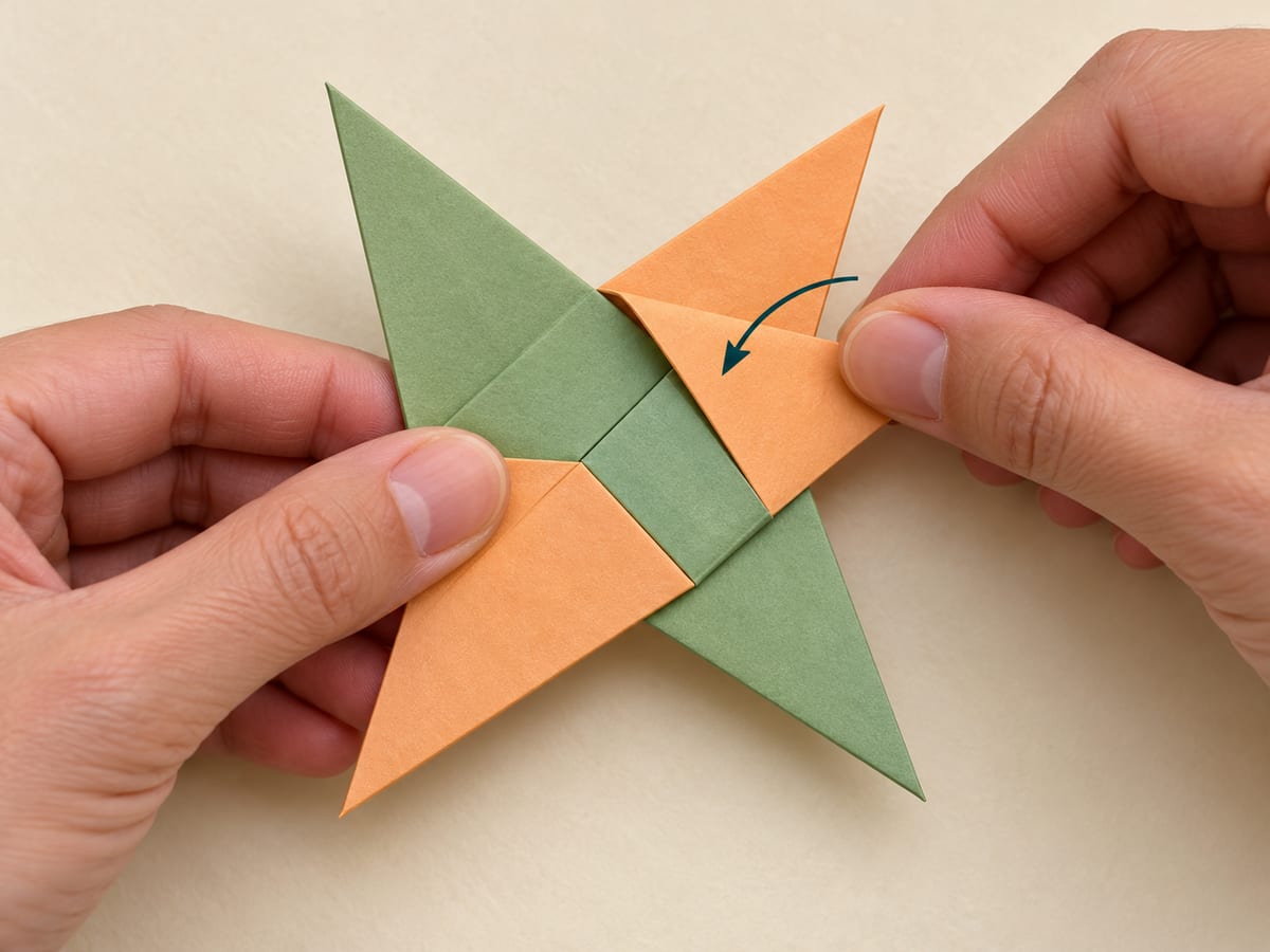 origami ninja star step 12: fold the remaining two points across the center, tuck them into the open pockets, and flatten the star, hands visible