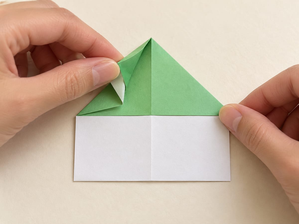 origami frog step 6: fold the left corner of the upper triangle toward its top point, hands visible