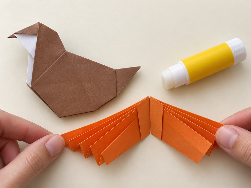 origami turkey step 10: fold the pleated stack in half; glue the two inside end panels together, hands visible
