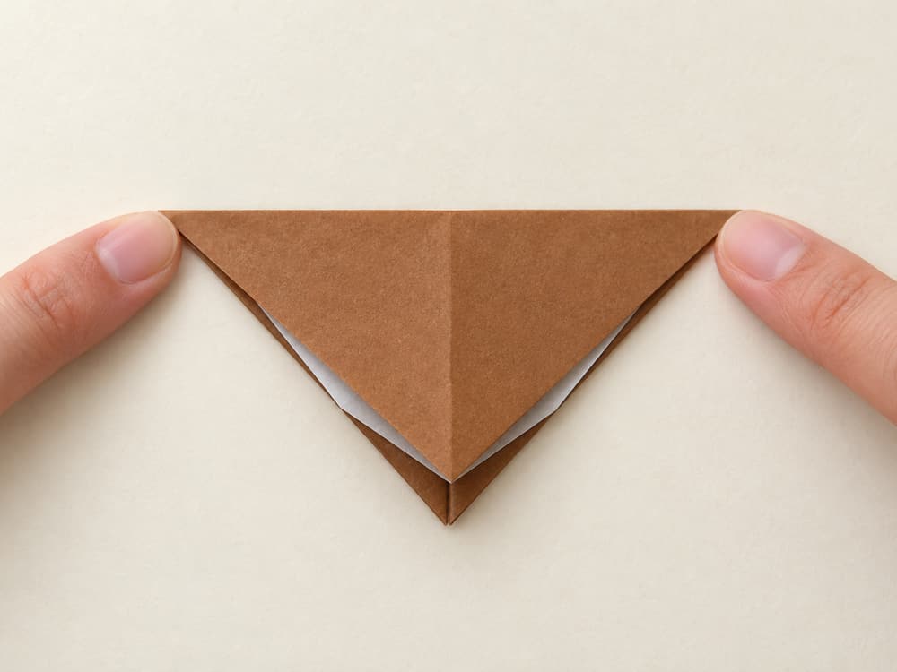 origami turkey step 4: turn the kite over and bring its long top point down to the bottom point, hands visible