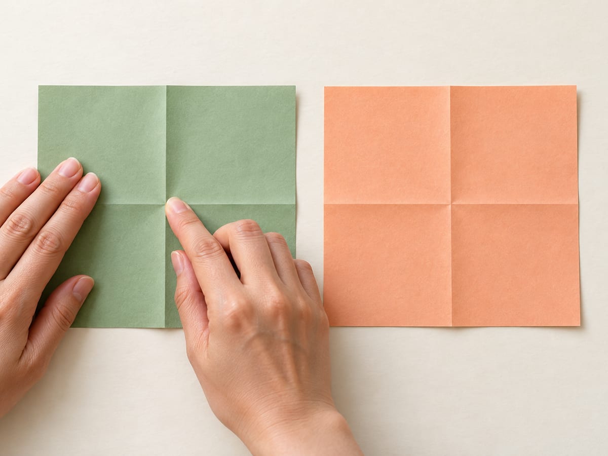 origami ninja star step 1: fold each square in half vertically and horizontally, then reopen both sheets, hands visible