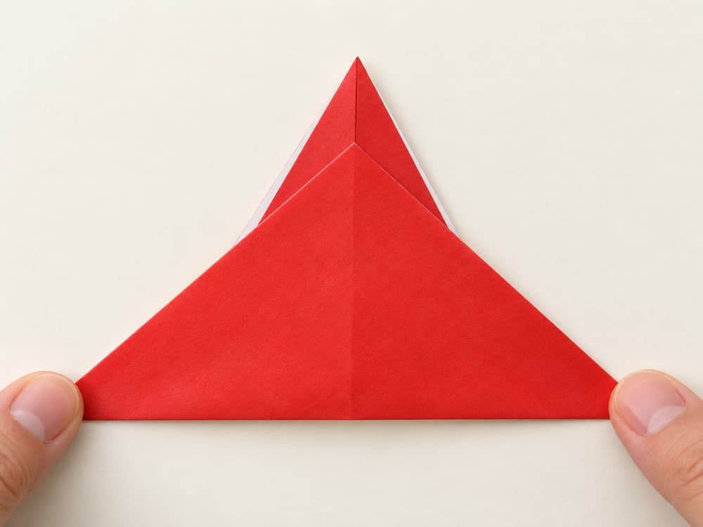 origami santa step 5: turn the whole triangle over with its point still facing upward, hands visible