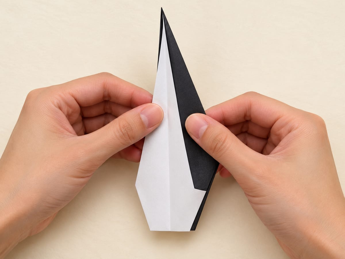 origami penguin step 6: fold the body in half along its center crease, keeping the broad belly visible outside, hands visible