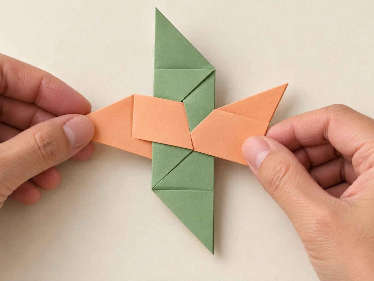 origami ninja star step 9: turn the first piece over and place the second across it, with their center sections overlapping at right angles, hands visible