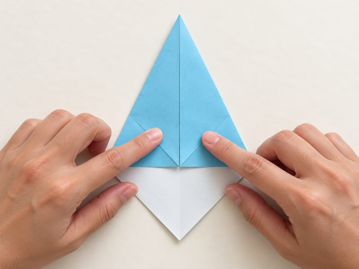 origami shark step 4: fold the upper-left sloping edge to the center to complete a narrow kite, hands visible