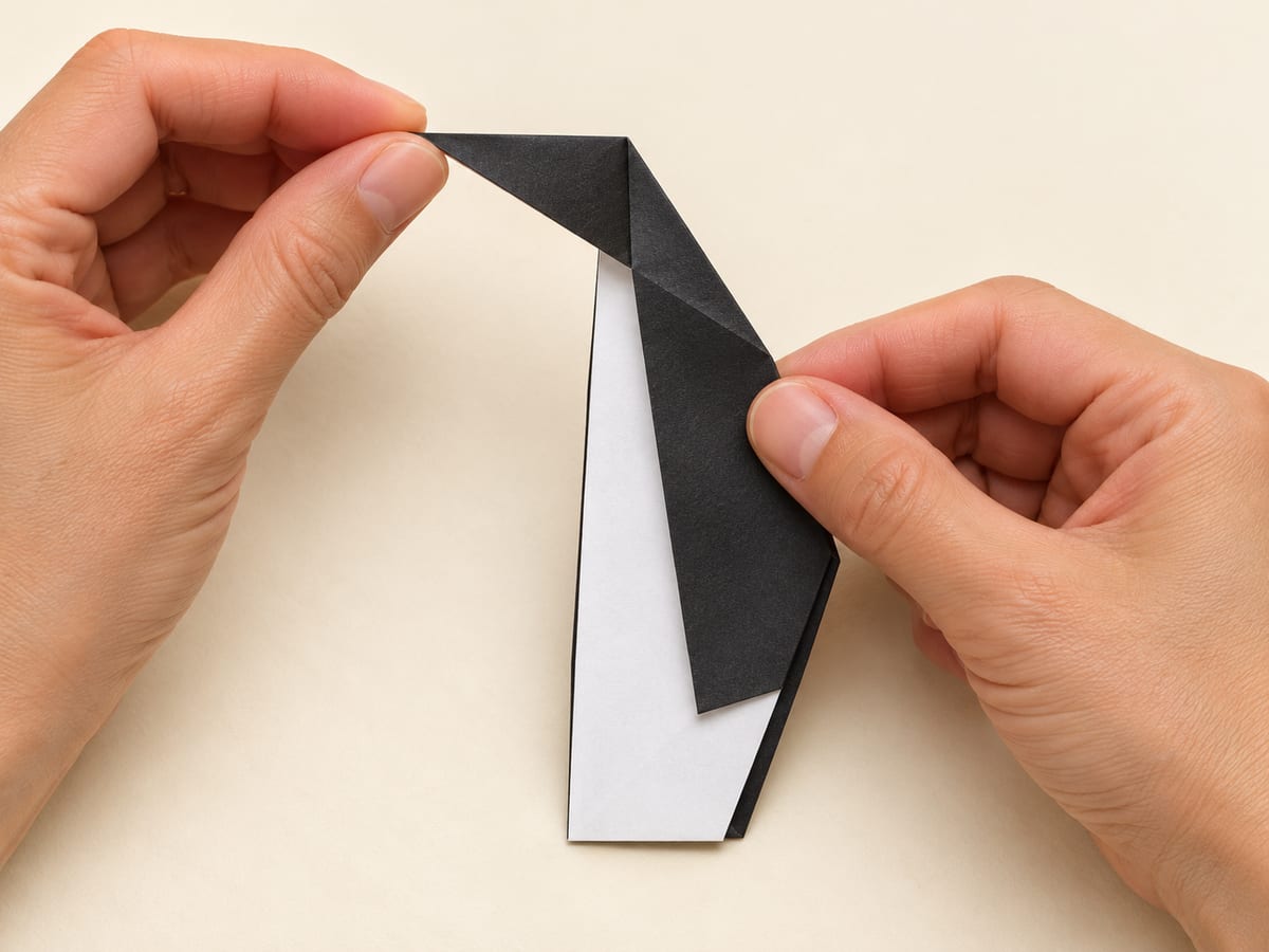origami penguin step 7: fold the upper tip sideways to make a short head, crease in both directions, then reopen, hands visible