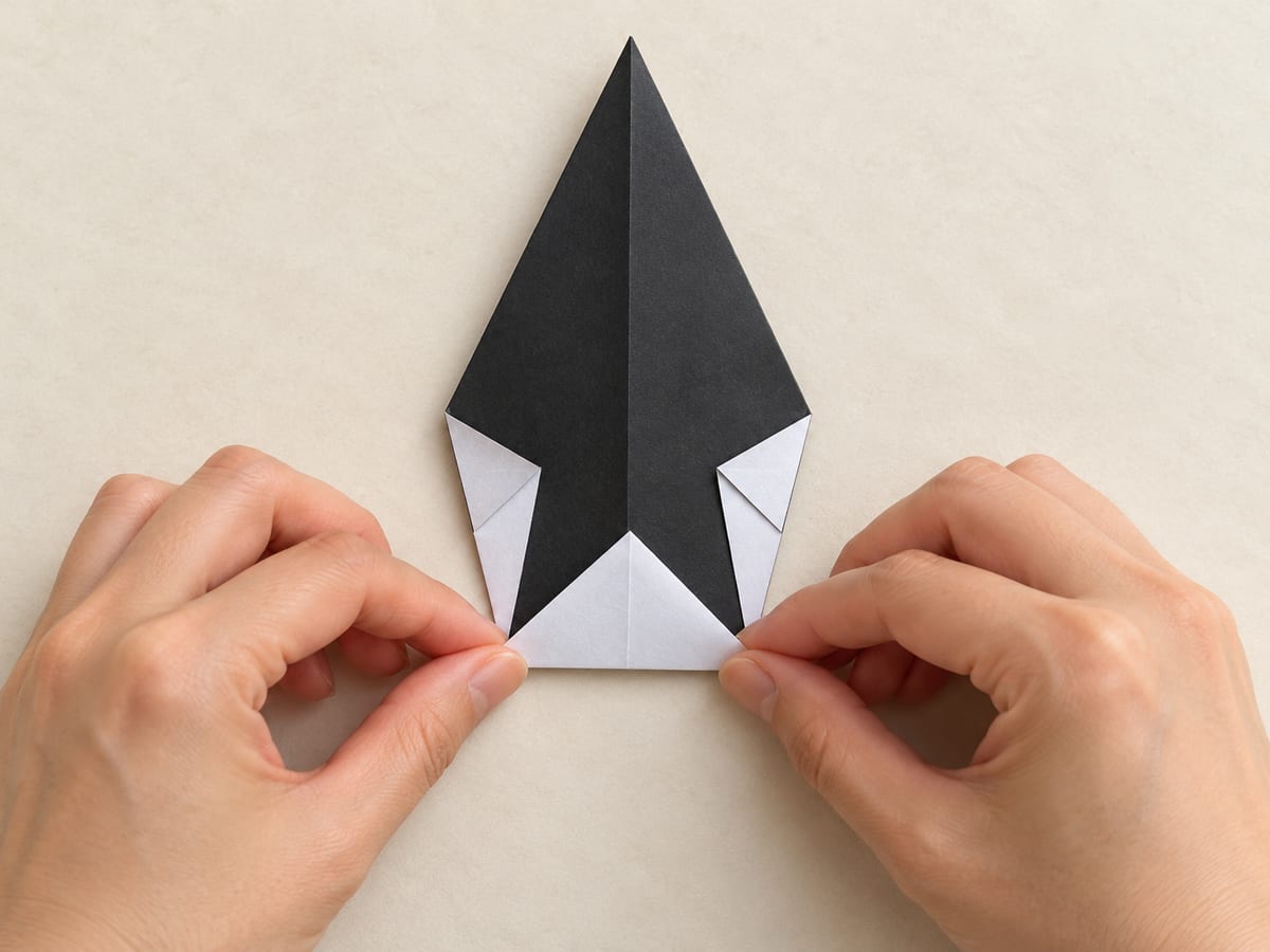origami penguin step 5: lift the bottom point to the lower ends of the side flaps and press the new base crease, hands visible