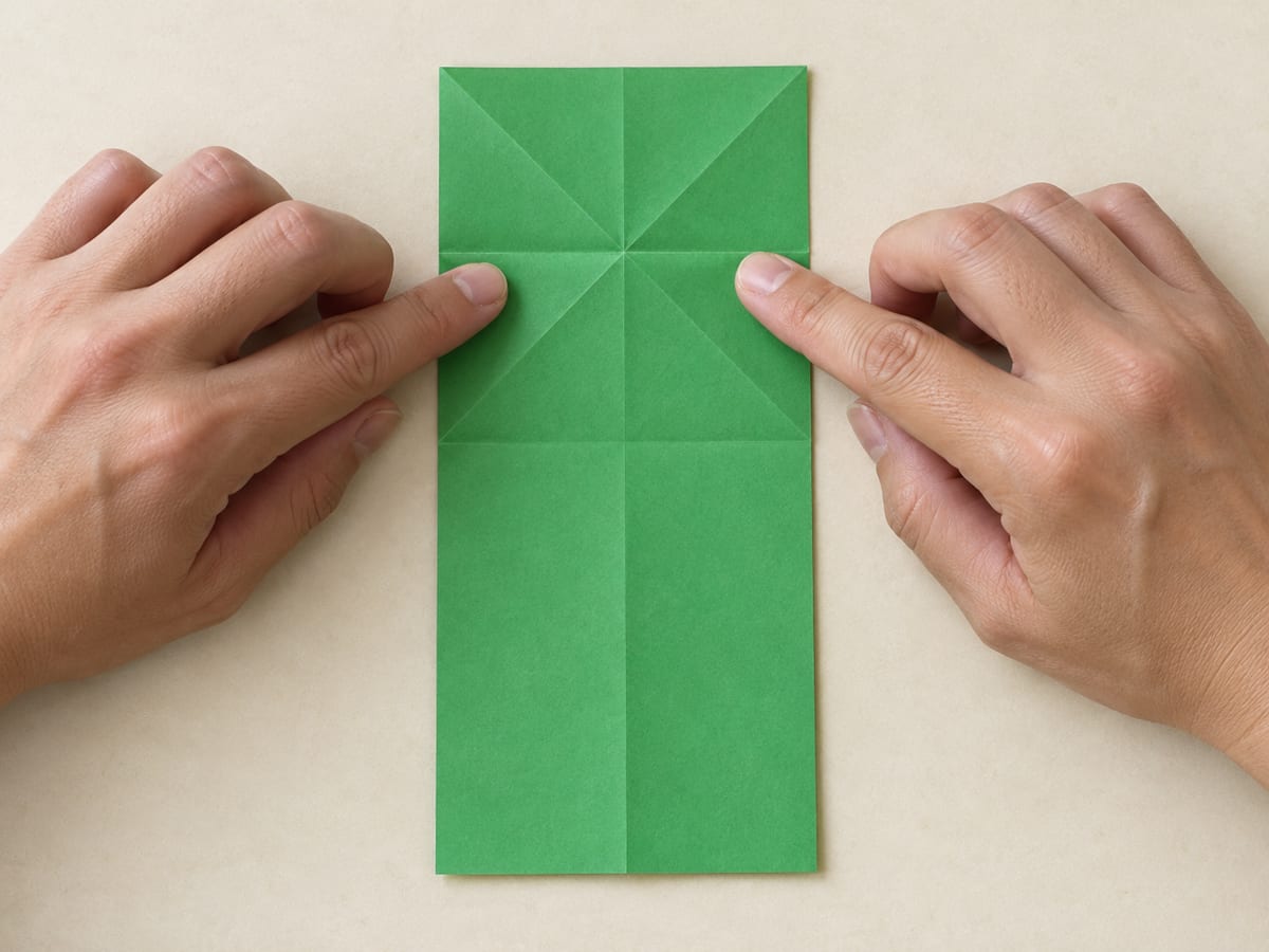origami frog step 4: turn the sheet over and crease across the center of the X, hands visible