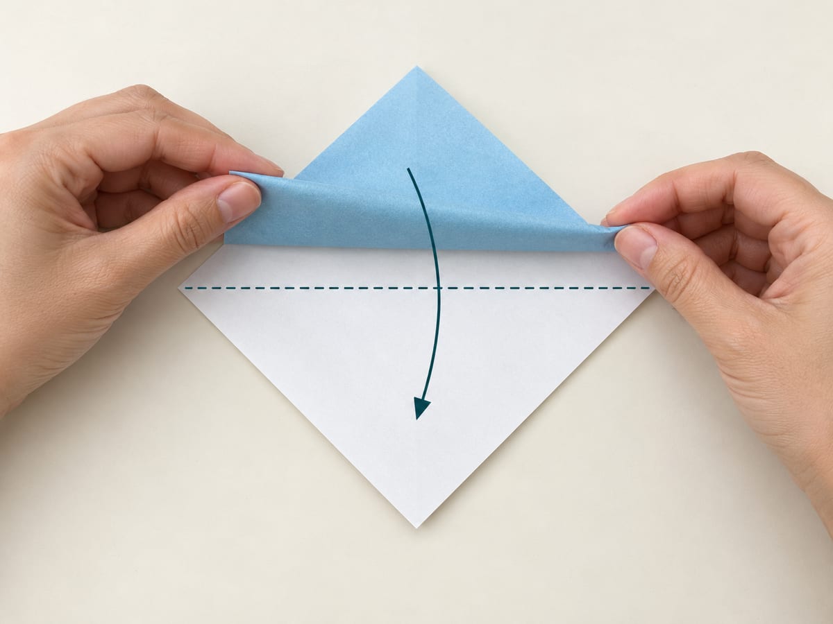 origami shark step 1: fold the top corner onto the bottom corner to make a horizontal guide, hands visible