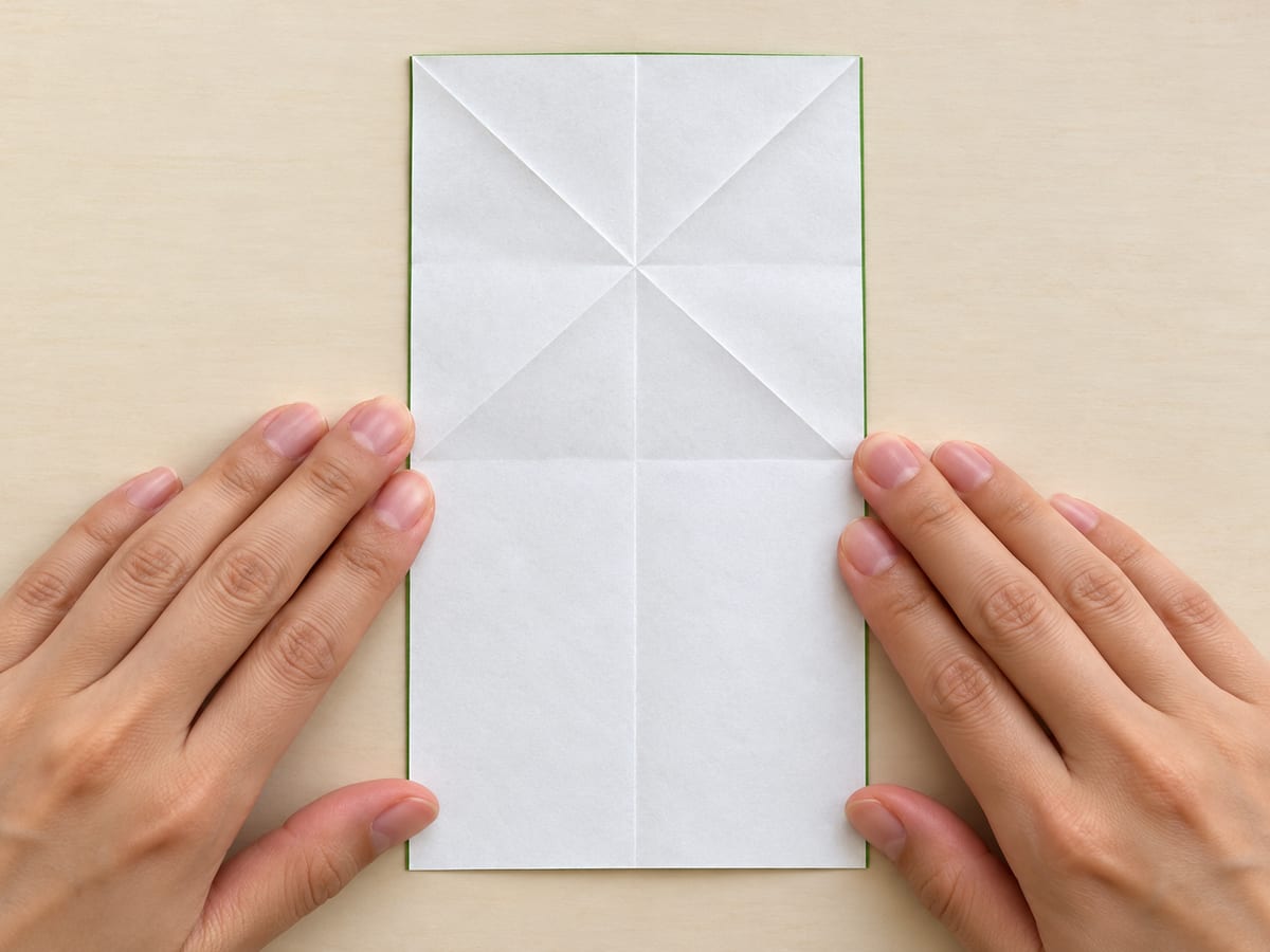 origami frog step 3: repeat with the upper-right corner and left edge; unfold to reveal an X across the top square, hands visible