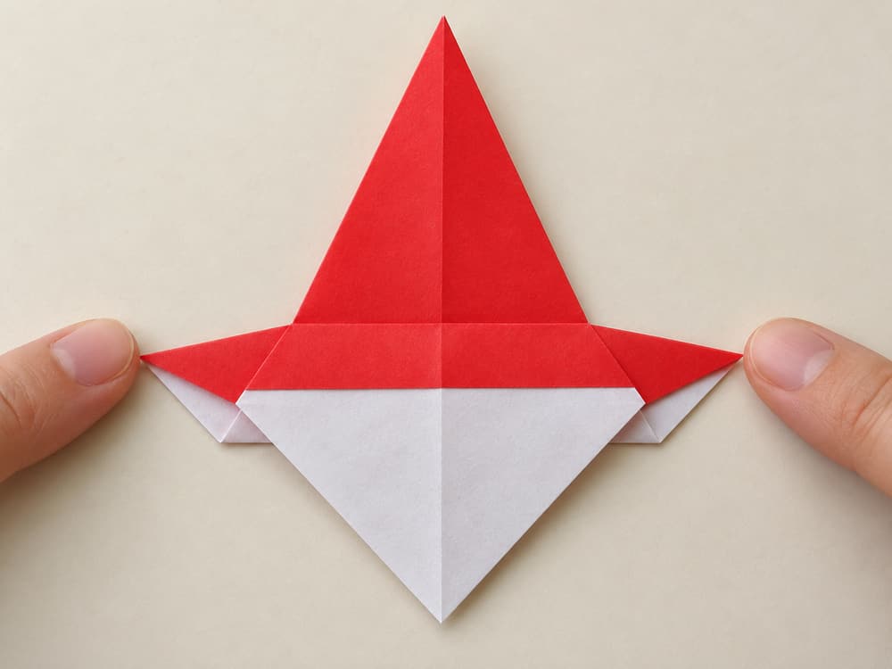 origami santa step 6: bring only the broad front point down to the bottom edge, revealing its white reverse, hands visible