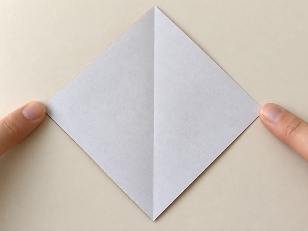 origami turkey step 1: place the brown square white side up as a diamond; fold left point to right point, then reopen, hands visible
