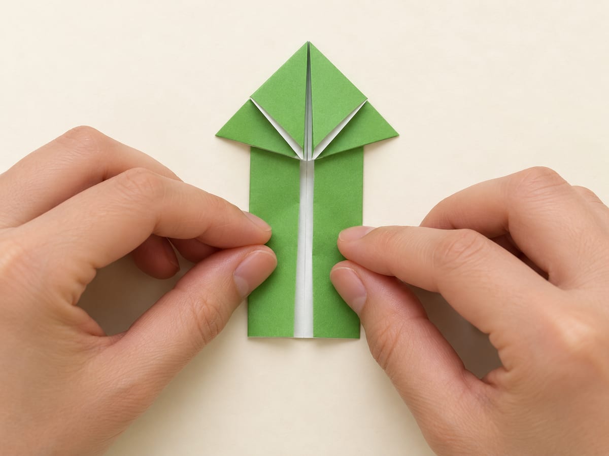origami frog step 8: fold both long side edges inward to the center, keeping the front legs free, hands visible
