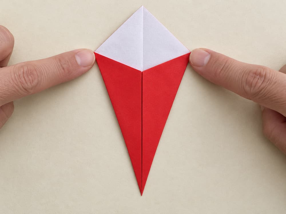 origami santa step 3: bring the lower-left sloping edge to the same crease, hands visible