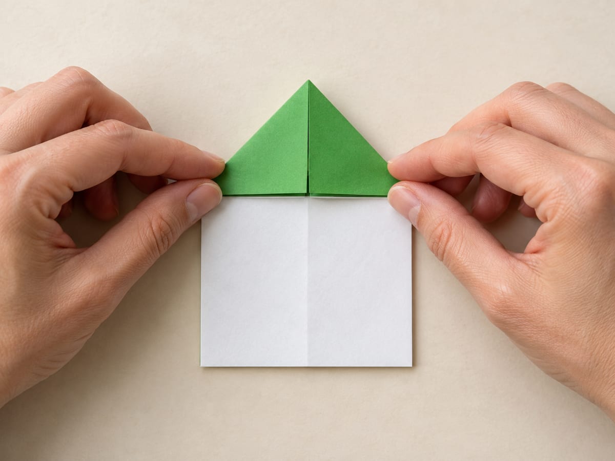 origami frog step 5: turn back over; push the sides of the X inward and flatten the top into a triangle, hands visible