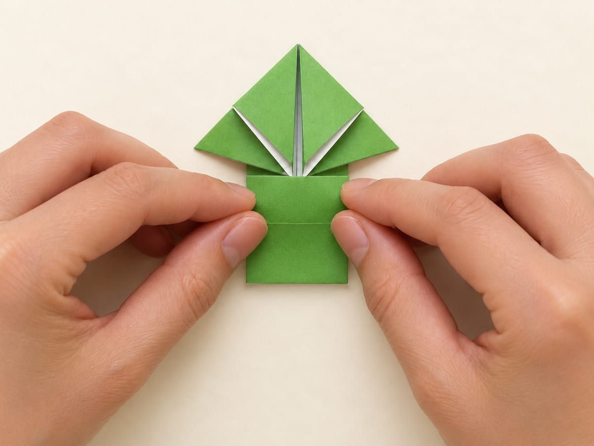 origami frog step 9: bring the bottom edge upward to the center of the small diamond formed by the front legs, hands visible